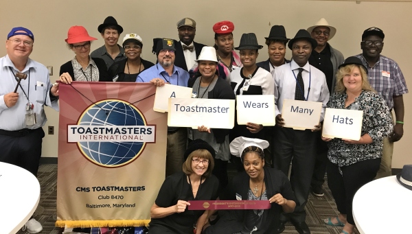 Toastmasters Club 8470 members wearing hats on Hat Day and showing the slogan A Toastmaster Wears Many Hats
